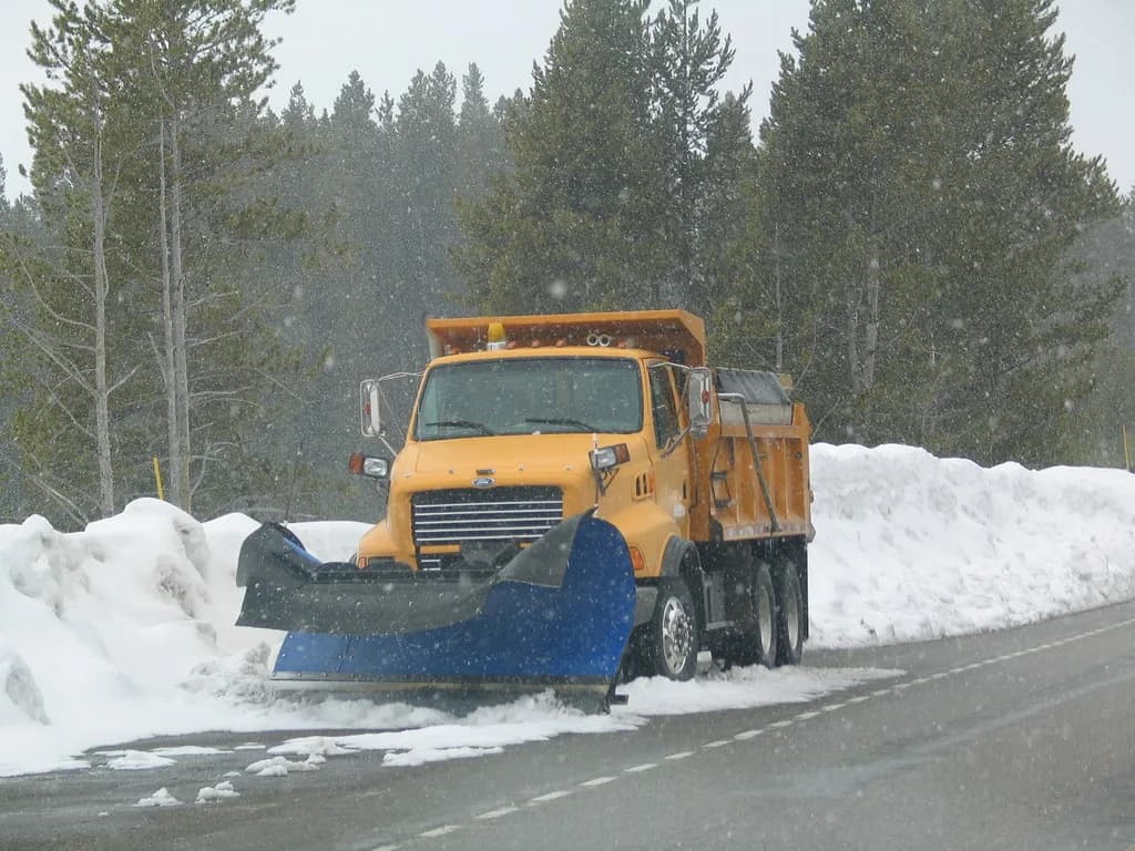 A plow truck with its blade down, pushing snow while it is still falling